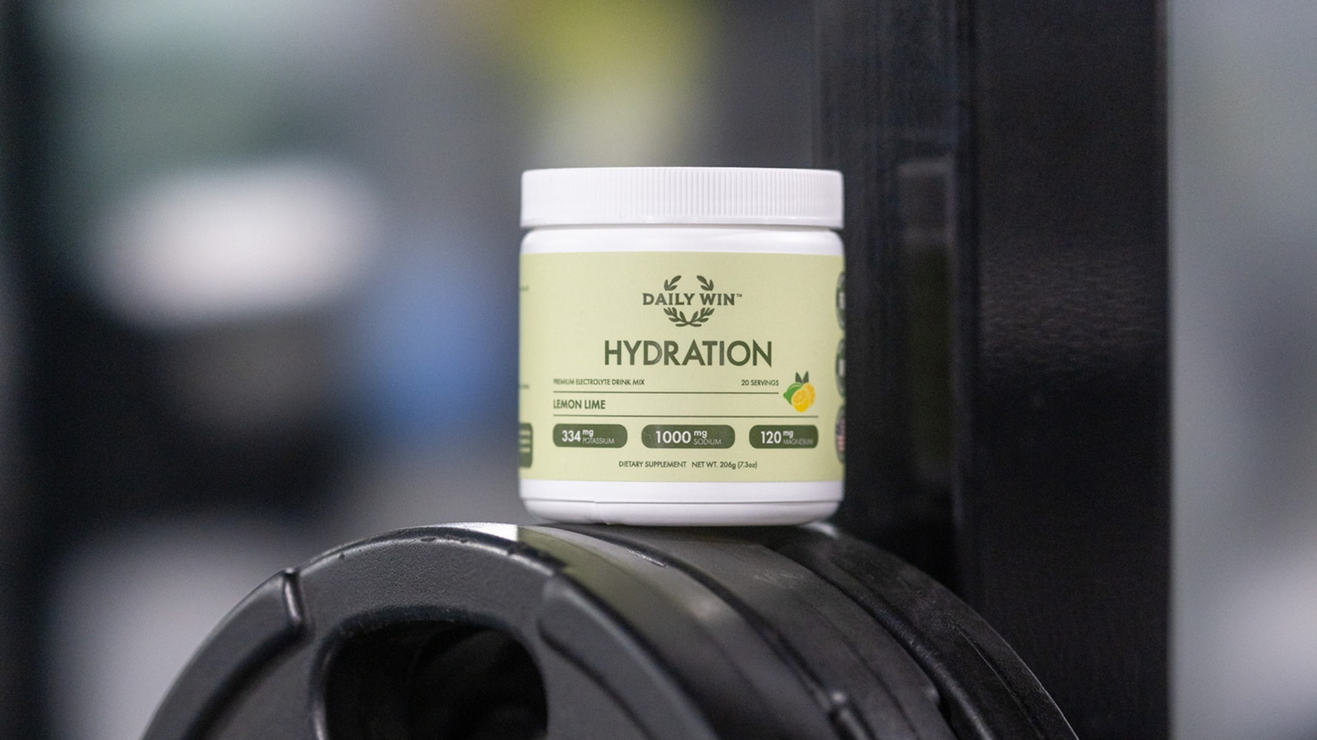 Daily Win Lemon Lime electrolyte tub on a weight plate in a gym
